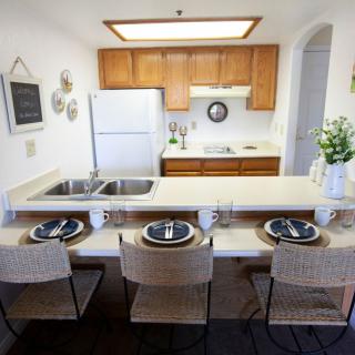 A cozy kitchen setup with a dining area featuring bar stools and place settings, complemented by white appliances and wooden cabinets.