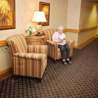 A cozy waiting area featuring striped chairs and a lamp, with a senior citizen reading in the corner.