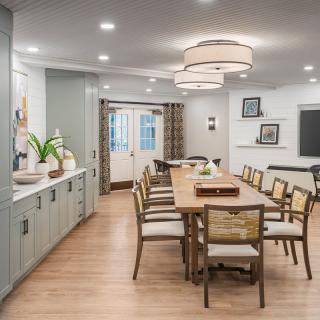 A modern dining room with a long wooden table, surrounded by stylish chairs, featuring elegant lighting and wood flooring.