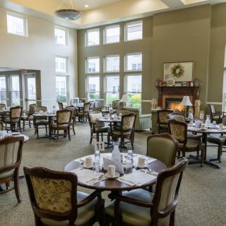 An elegant dining room with neatly set tables, comfortable chairs, large windows, and a cozy fireplace.