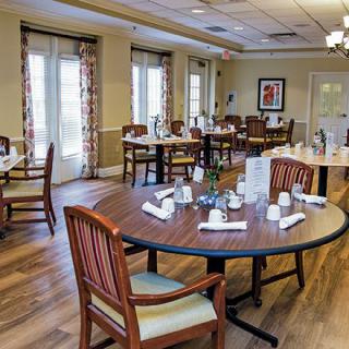 A well-organized dining room with tables and chairs set for a meal, featuring elegant wooden flooring and ample natural light.
