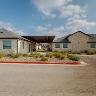 A view of a modern building exterior with a covered driveway and landscaped surroundings under a cloudy sky.