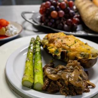 A plated meal featuring grilled asparagus, stuffed potato, and saut�ed mushrooms, with grapes and bread in the background.