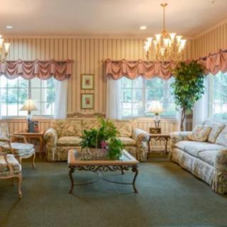 A traditional living room with elegant furnishings, including patterned sofas, a glass coffee table, chandeliers, and houseplants.