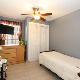 A cozy, well-organized bedroom with a single bed, dresser, and ceiling fan.