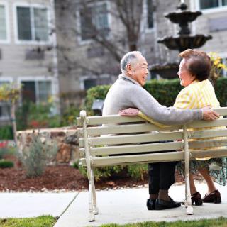 An elderly couple sits together on a park bench, enjoying the serene garden view.