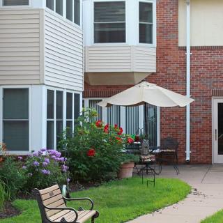 A cozy patio area with a garden, bench, and umbrella next to a brick building.
