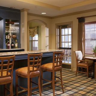 A cozy bar interior featuring a counter with wooden chairs and a side table by the windows.