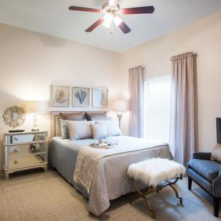 A cozy and well-decorated bedroom featuring a bed with stylish bedding, bedside lamps, mirrored nightstand, and soft lighting.