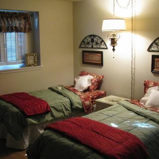 A cozy bedroom featuring two twin beds with green bedding and red accents, complemented by warm lighting.