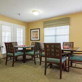 A cozy dining area with tables and chairs, decorated with warm colors and natural light from windows.