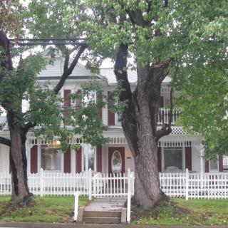 A charming two-story house with a white picket fence and large trees in the front yard.