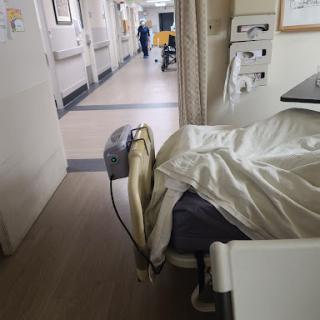 A view inside a hospital patient room, showcasing the bed with a patient and healthcare staff in the hallway.