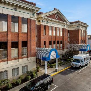 A hospital building with a covered entrance and parked vehicles.