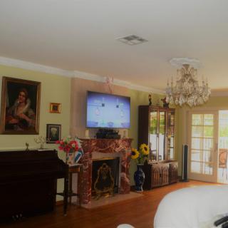 A cozy living room featuring a chandelier, fireplace, and piano, with decorative elements including sunflowers and a wall-mounted television.
