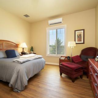 A cozy bedroom with a bed, armchair, and window, illuminated by warm lighting.