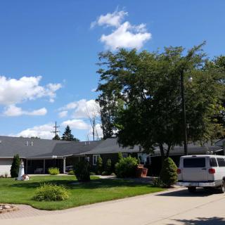 A suburban house with a driveway, trees, and a parked vehicle under a blue sky with clouds.