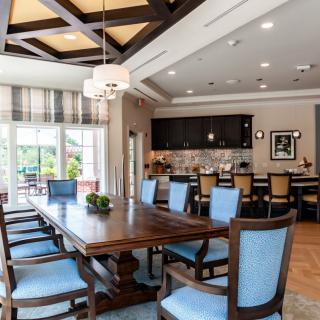 A stylish dining room with a large wooden table and blue upholstered chairs, connected to an open kitchen area.