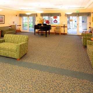 A cozy lounge area featuring sofas, a piano, and large windows.