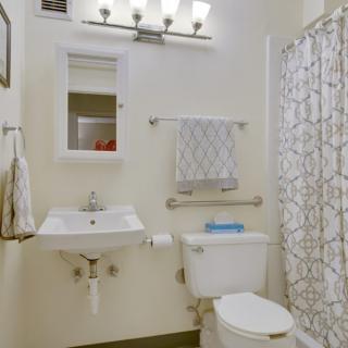 A well-lit bathroom with a sink, mirror, toilet, and shower area.