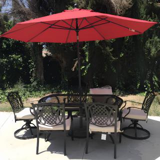 A patio set with a red umbrella and chairs in a garden setting.