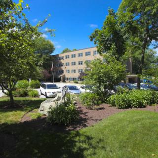 A sunny day with a building surrounded by trees, cars, and well-maintained landscaping.