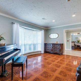 A spacious living room featuring a piano, hardwood floors, and large windows with drapes.