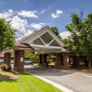 A covered entrance with a brick structure and a driveway, surrounded by trees on a sunny day.