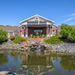 A charming building with a symmetrical facade surrounded by lush greenery and a tranquil pond reflecting its structure.