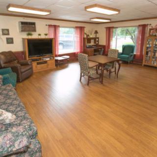 A cozy living room with wooden flooring, featuring a television, sofa, chairs, and a bookshelf.
