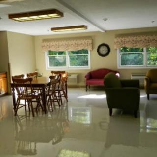 A bright living room with furniture, including chairs, a table, and a sofa, illuminated by natural light from large windows.
