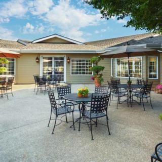 A sunny outdoor patio area with tables, chairs, and umbrellas in front of a building.