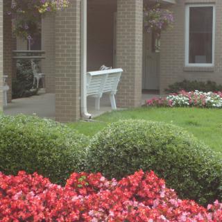 A well-maintained garden with colorful flowers and a white bench near a brick building.