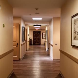 A well-lit hallway with doors on either side, featuring wooden flooring and framed artwork.
