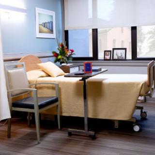 A clean and well-lit hospital room with a bed, chair, and flowers on the table.