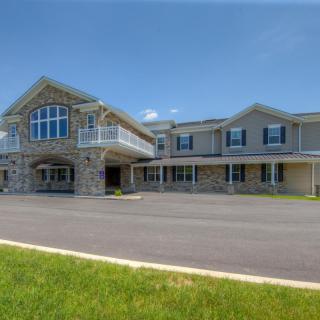 A large stone and siding house with multiple windows, a balcony, and a spacious driveway under a clear blue sky.