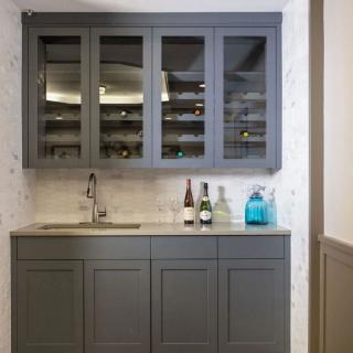 A modern kitchen setup with a grey cabinet, countertop, sink, and bottles displayed.