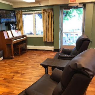 A cozy lounge area featuring comfortable seating, a piano, and natural light coming through the windows.