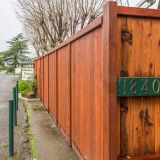A wooden fence with an address number displayed on it, lining a street.