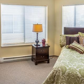 A cozy bedroom with a bed, nightstand, and lamp by the window.