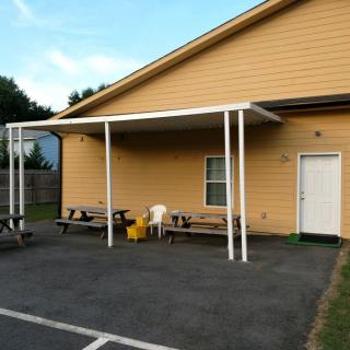 A building with an awning, benches, and chairs on the pavement.