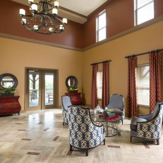 A spacious living room with patterned chairs, a chandelier, and large windows.