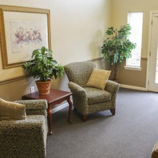 A cozy living room with two armchairs, a small table, potted plants, and a wall painting.