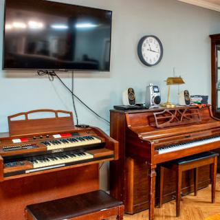 A cozy living room featuring a vintage organ and piano, along with a television and clock.