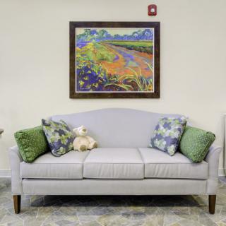 A cozy living room setup featuring a light gray sofa with decorative cushions, accompanied by a vibrant landscape painting on the wall.