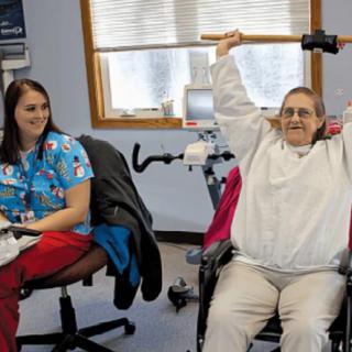 A senior woman engages in physical therapy exercises under the supervision of a healthcare professional.