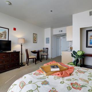 A comfortable hotel room featuring a bed with floral bedding, a TV, and a cozy seating area.