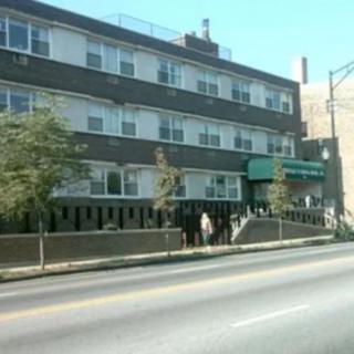A city street view featuring a multi-story building with trees along the sidewalk.