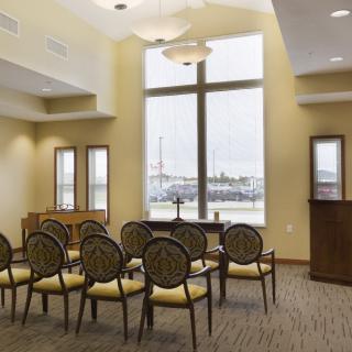 A small, well-lit meeting or lecture room with chairs arranged in rows and large windows overlooking an outdoor view.