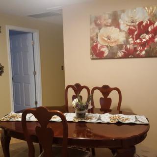 A cozy dining room with a wooden table and chairs, decorated with a floral painting on the wall.